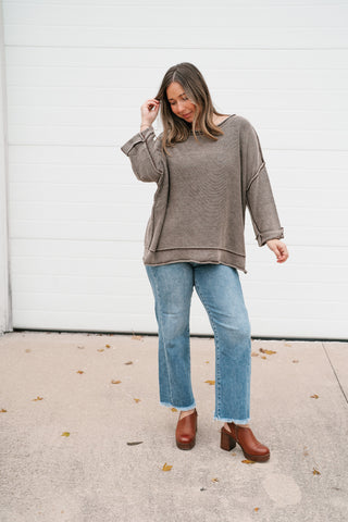 Model with a hand in her hair wearing the relaxed brown knit dolman sweater and jeans