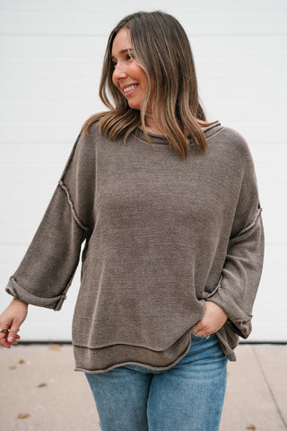 Smiling model in the relaxed brown knit sweater showing the dolman sleeves and layered hem