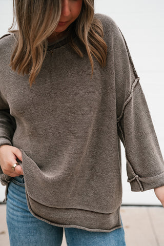 Close-up of the washed brown lightweight knit sweater showing the rolled neckline and exposed seams