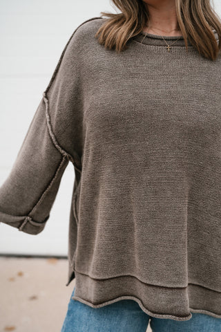 Close-up of the brown dolman sweater's textured knit, exposed seams and layered hem