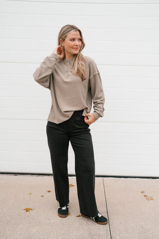 Model with a hand in her hair wearing the mocha thermal henley top and black wide-leg pants