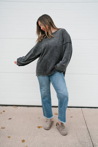 Model reaching out one arm to show the long drop-shoulder sleeve of the oversized charcoal pullover sweater