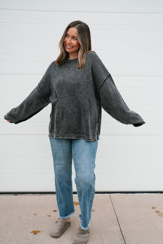 Model with arms out showing the slouchy oversized fit of the charcoal mineral-wash sweater