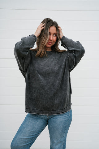 Model with hands in her hair wearing the charcoal oversized crew neck knit sweater with jeans