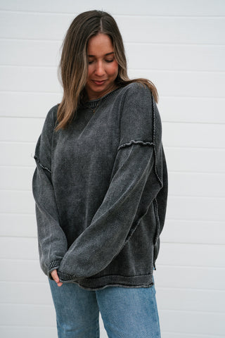 Waist-up view of the charcoal oversized knit sweater with exposed seam details on the drop shoulders
