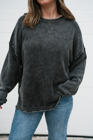 Close-up front view of the charcoal washed knit sweater showing the crew neckline, exposed seams and ribbed hem
