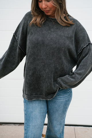 Close-up of the charcoal knit sweater's washed texture, raw seam detail and long sleeves