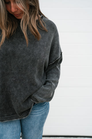 Close-up of the charcoal mineral-wash knit, exposed shoulder seam and ribbed hem