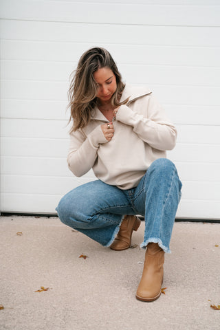 Model crouching in the cream quarter zip pullover sweater with light wash jeans and tan boots