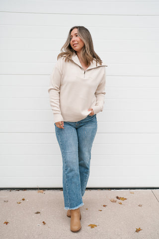 Model walking in the relaxed cream quarter zip pullover sweater with jeans and booties
