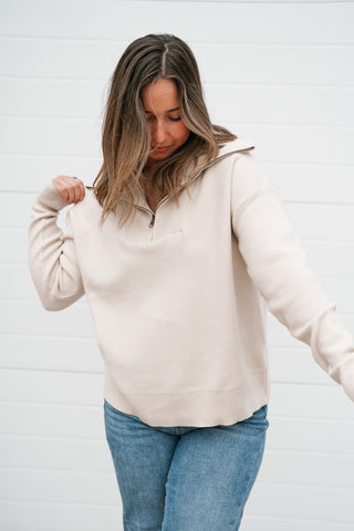 Model pulling at the collar of the cream quarter zip pullover showing the soft knit