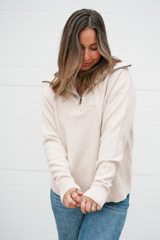 Front view of the cream quarter zip sweater with long sleeves and ribbed cuffs worn with jeans