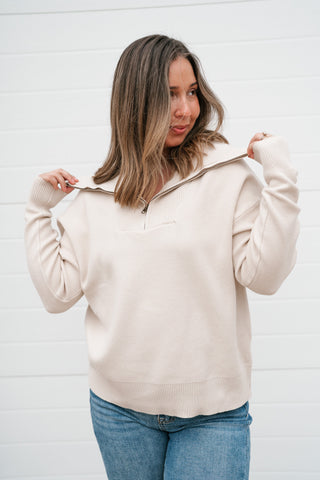 Model holding the collar of the cream quarter zip sweater to show the oversized fold-over collar