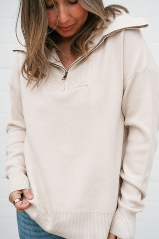 Close-up of the cream quarter zip sweater showing the wide spread collar and metal zipper