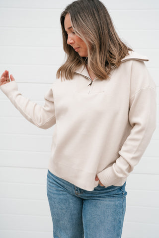 Woman wearing the Simply Yours relaxed cream quarter zip pullover sweater with light wash jeans