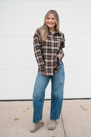 Smiling model in the oversized chocolate plaid button down top with hands in her jeans pockets