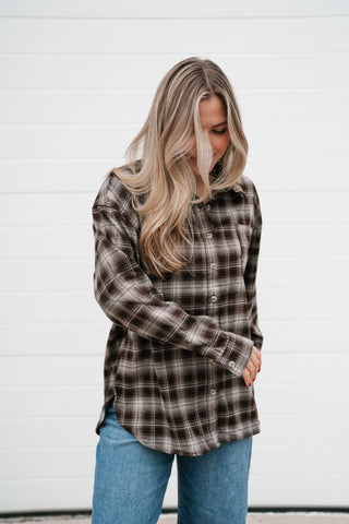 Side view of the chocolate brown plaid shirt showing the long sleeves and curved hem