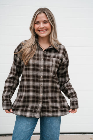 Model holding the hem of the oversized brown plaid button down shirt