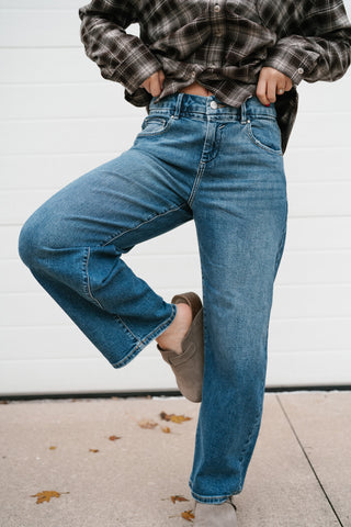 Model lifting one knee to show the relaxed curved leg of the medium wash barrel jeans