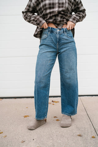 Front view of the high rise medium wash barrel jeans styled with a brown plaid shirt and clogs
