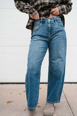 Angled view of the medium blue barrel leg jeans showing the curved, relaxed leg