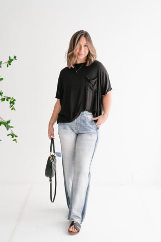 Woman wearing Driftline light wash wide-leg printed denim jeans with dark side stripes, paired with a black pocket tee and sandals in a bright studio setting.