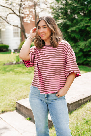 A woman outdoors wearing a trendy pink and mocha brown striped boxy t-shirt paired with light-wash denim jeans.