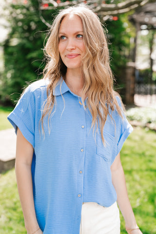 Woman wearing a blue shirt outdoors with greenery in the background