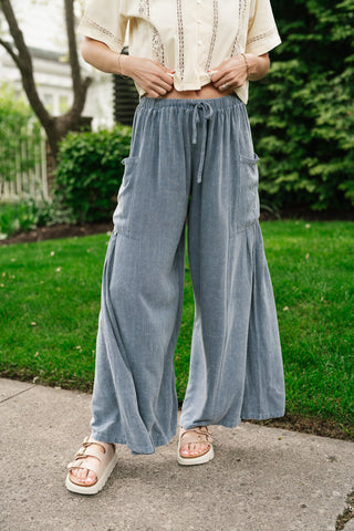 Woman wearing dusty blue high-waisted wide-leg cargo pants with drawstring waist and textured fabric standing on a sidewalk.