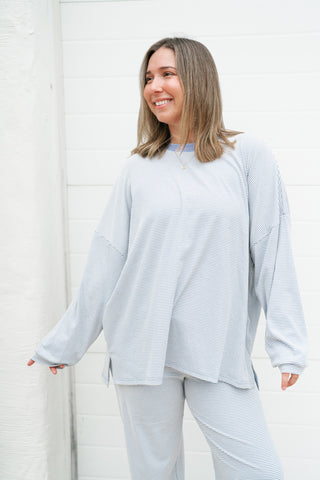 A woman wearing a light blue and white striped long-sleeve top and matching pants, standing against a white paneled wall.