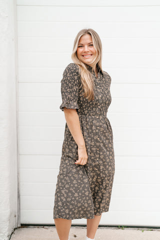 A woman modeling a short-sleeve midi dress with a brown and beige geometric pattern, standing in front of a white paneled garage door.