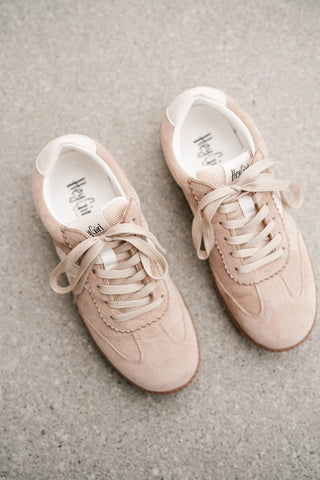 Top-down view of Hey Girl brand light beige suede sneakers with scalloped trim and white accents on a neutral stone background.