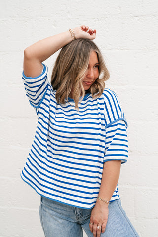 A woman wearing the Daydreamer Oversized Stripe Tee in royal blue and white, featuring a contrast crew neckline and dropped shoulders, paired with light-wash denim jeans.