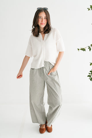 Woman wearing a white short-sleeve textured knit button-down polo and striped barrel-leg pants for a coastal chic summer look.