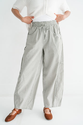 Woman wearing high-waisted wide-leg pinstripe trousers with a drawstring waist and white knit cardigan.