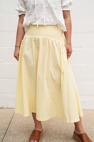Model wearing the Sunwashed Cotton Drop Waist Midi Skirt in pale yellow, featuring a flattering drop waistline and a flowy, breathable 100% cotton fabric.