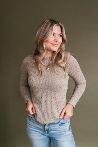 Woman wearing the Faded Florals Long Sleeve Ribbed Top in taupe with a subtle brown floral print, styled with light wash jeans and a beaded necklace.