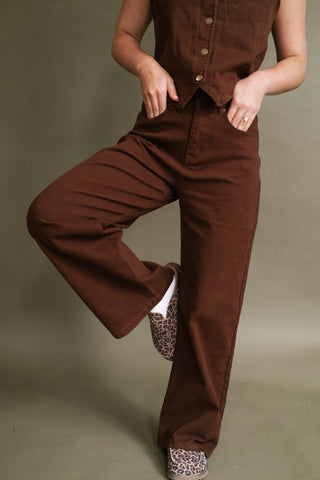 Woman wearing chocolate brown high-rise wide-leg jeans with a matching brown button-front vest and leopard print sneakers.