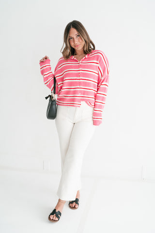 A woman wearing a pink and red striped polo-collar cardigan paired with white wide-leg pants and black sandals, standing against a clean white background.