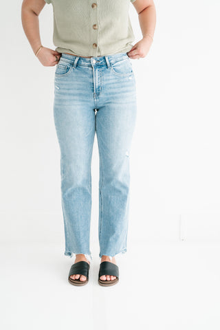 Woman wearing light wash high-waisted straight-leg jeans with a raw hem and black slide sandals.