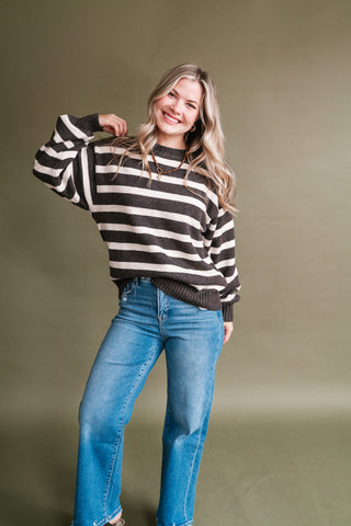Woman wearing a brown and ivory striped knit crewneck sweater with blue high-rise wide-leg jeans.